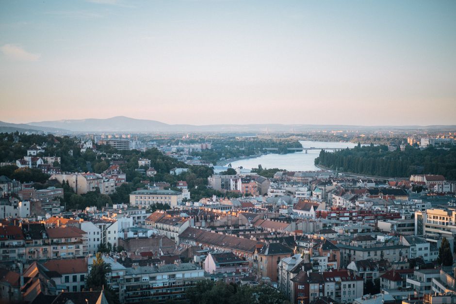 An aerial perspective of a sprawling historic city built along a major river, showcasing bridges, famous landmarks, and green spaces bathed in soft light.