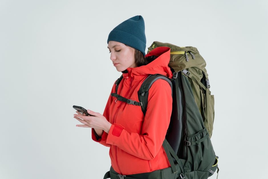 A solo female backpacker, smiling, standing in a vibrant city square, looking at her phone for directions with historic European architecture in the background.
