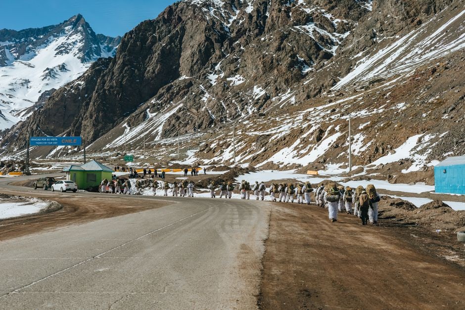A long-distance bus parked at a remote mountain border crossing between Argentina and Chile, with passengers getting off to go through immigration.