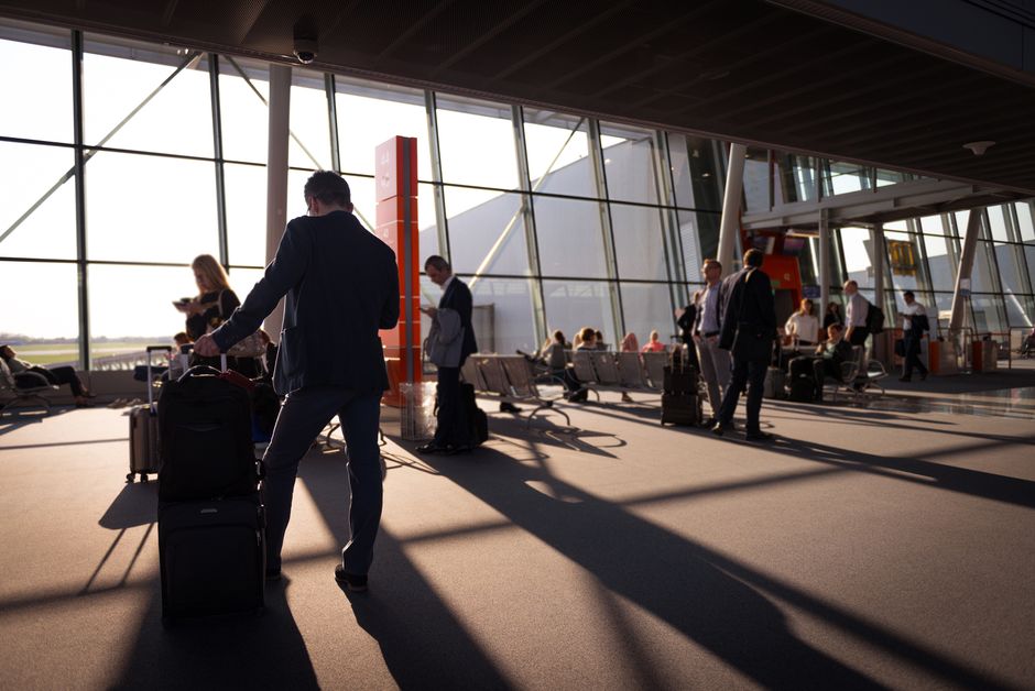 Woman smartly dressed in a blazer and trousers, carrying a sleek carry-on suitcase through an airport terminal, looking confident and ready for a business trip.