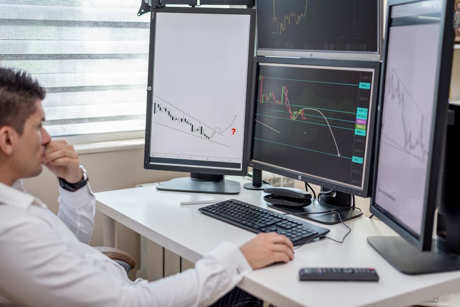 A focused businessman in an office environment, looking at multiple digital screens displaying various data and analytics, representing strategic decision-making.