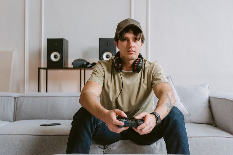 A person comfortably lounging on a sofa, casually holding a controller and focusing on an engaging story game on a TV screen.