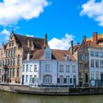 A picturesque cobblestone street in a historic European town, with colorful buildings lining a tranquil river and a few people strolling leisurely.