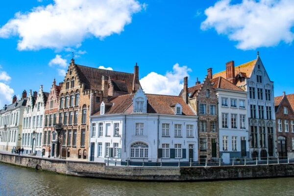 A picturesque cobblestone street in a historic European town, with colorful buildings lining a tranquil river and a few people strolling leisurely.
