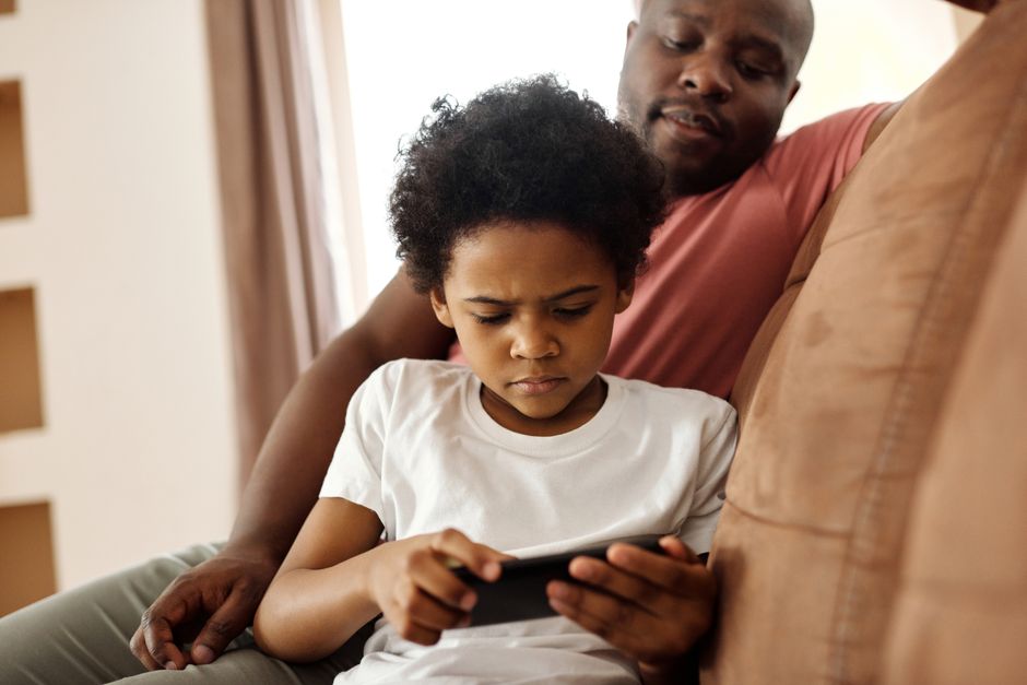 A parent and child sharing a moment while the child plays a mobile game on a tablet, emphasizing family awareness in mobile gaming.
