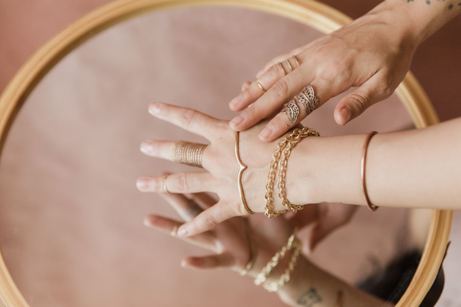 Close-up of a hand adorned with several thin, minimalist gold rings and a simple chain bracelet against a soft background, emphasizing everyday wear.