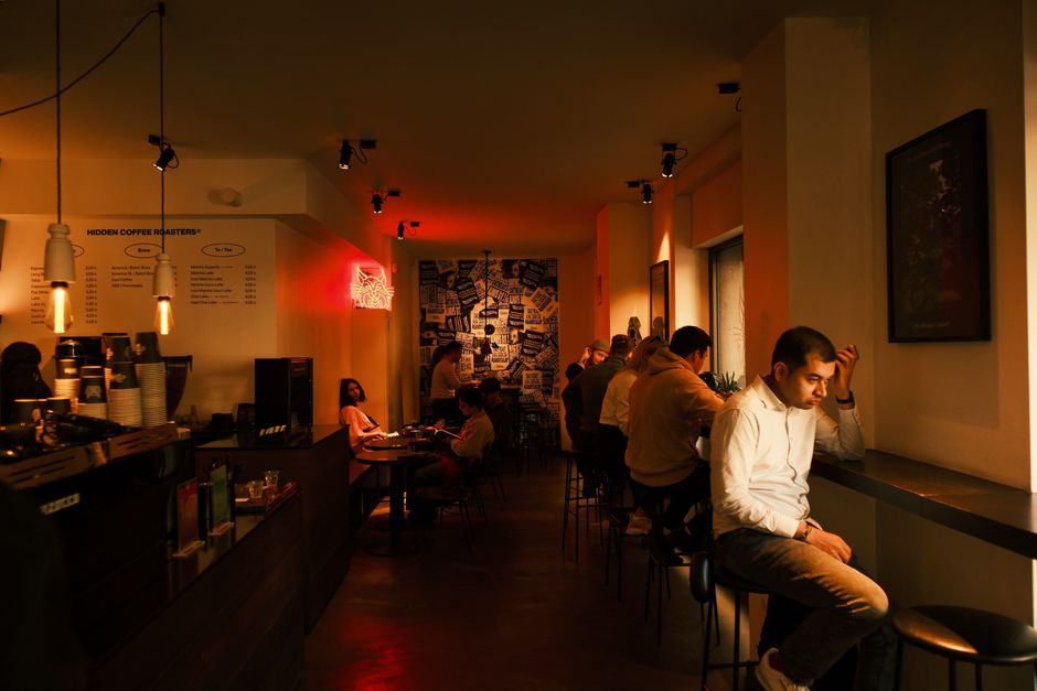 A vibrant, modern coffee shop interior in Barcelona with various patrons, including families with children, enjoying specialty coffees and pastries at tables and on comfortable couches.