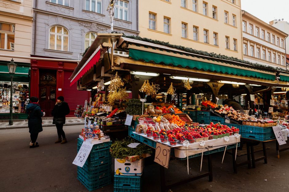 A vibrant display of colorful, seasonal fresh produce including bell peppers, tomatoes, and leafy greens on a market stall.
