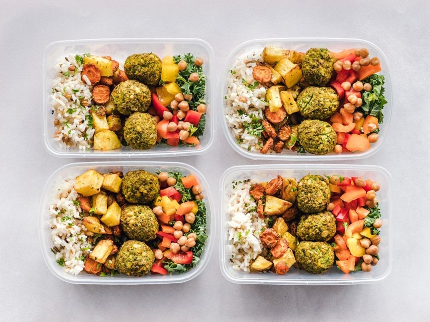 Several glass meal prep containers filled with various healthy food components like roasted vegetables, quinoa, and lean protein, arranged neatly on a kitchen counter.