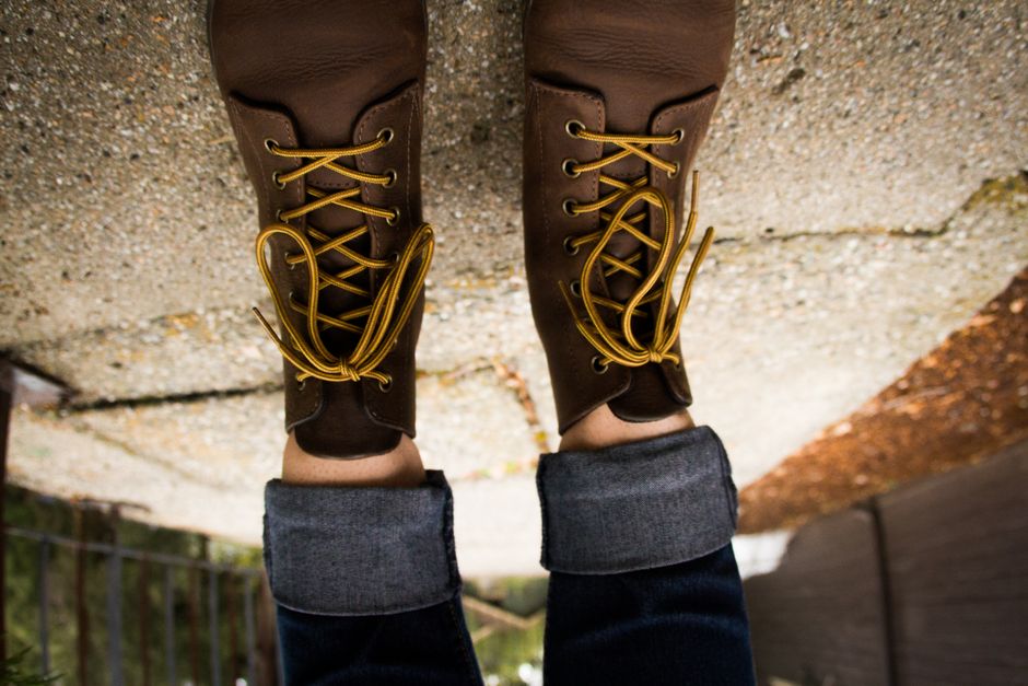 A close-up of stylish yet practical waterproof ankle boots on a person's feet, walking on a wet urban street with historic buildings in the background.