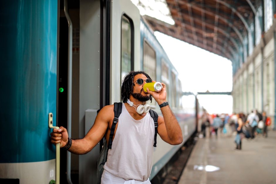 A person on a crowded commuter train taking a sip from a travel mug, looking out the window.