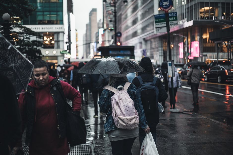 A person commuting through a rainy city street, wearing a sleek waterproof jacket and carrying a functional, water-resistant backpack, emphasizing practical fashion for urban travel.