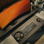 A clean, compact gaming setup in a small apartment corner, featuring a sleek monitor on a wall mount, a small form factor PC tucked neatly under the desk, and a simple ergonomic chair.