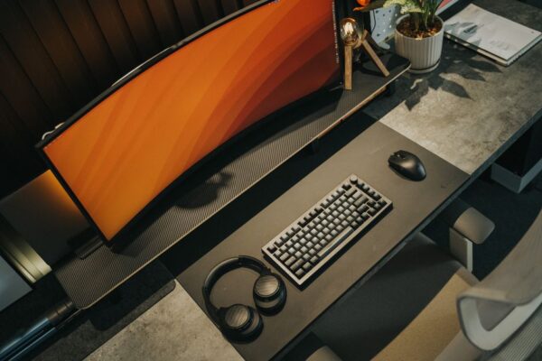 A clean, compact gaming setup in a small apartment corner, featuring a sleek monitor on a wall mount, a small form factor PC tucked neatly under the desk, and a simple ergonomic chair.