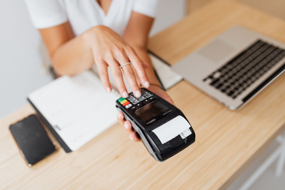 A close-up shot of a hand wearing a sleek, minimalist ring, tapping a contactless payment terminal at a cafe, demonstrating NFC jewelry.
