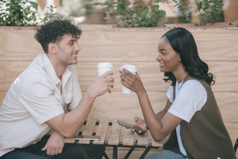 A couple sitting comfortably at an outdoor cafe, both wearing relaxed yet chic linen clothing, showcasing the enduring polish and comfort of summer linen outfits in a casual setting.