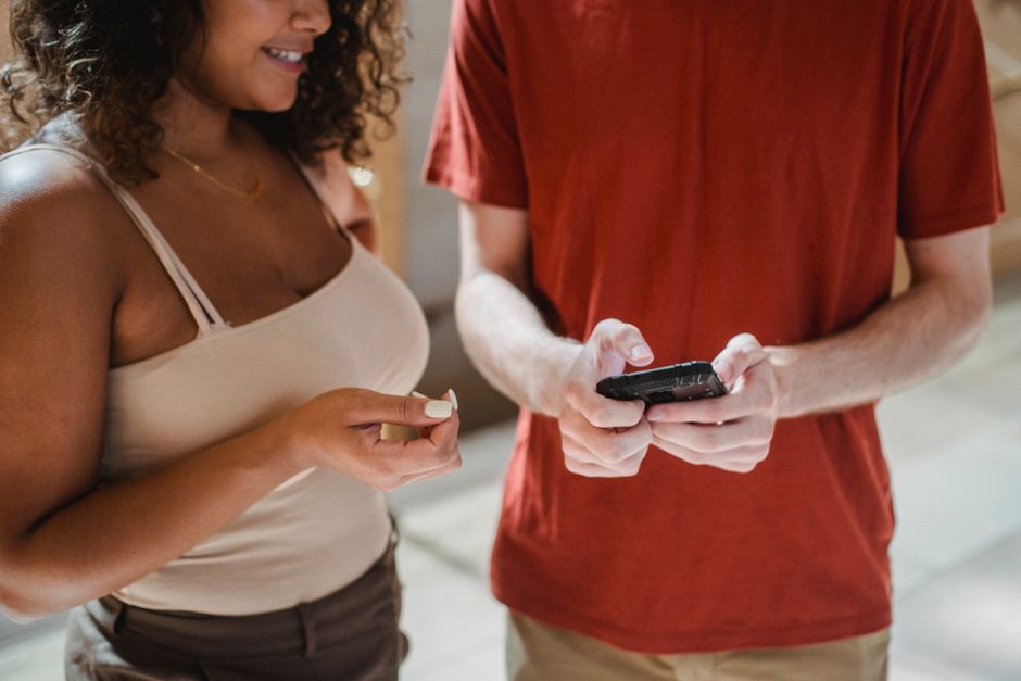 Two individuals, one local and one traveler, interacting while looking at a smartphone displaying a real-time translation app.