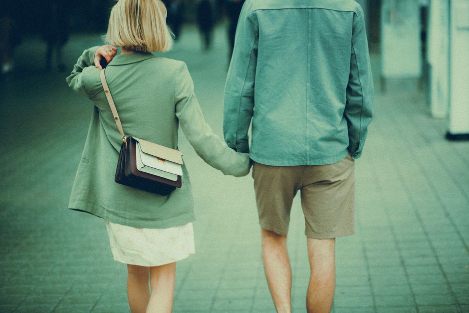 A couple walking through a European city street, both dressed in stylish, functional layers including light jackets and scarves, suitable for urban exploration.
