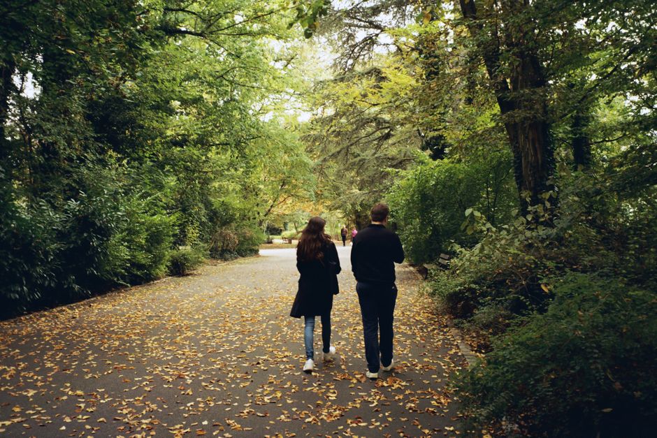A couple dressed in smart casual layers, enjoying a stroll on a sun-dappled autumn day in a European city, showcasing adaptable travel fashion.