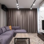 A bright, decluttered small apartment living room with a sofa, floor cushions, and warm lighting, ready for guests.