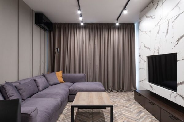 A bright, decluttered small apartment living room with a sofa, floor cushions, and warm lighting, ready for guests.