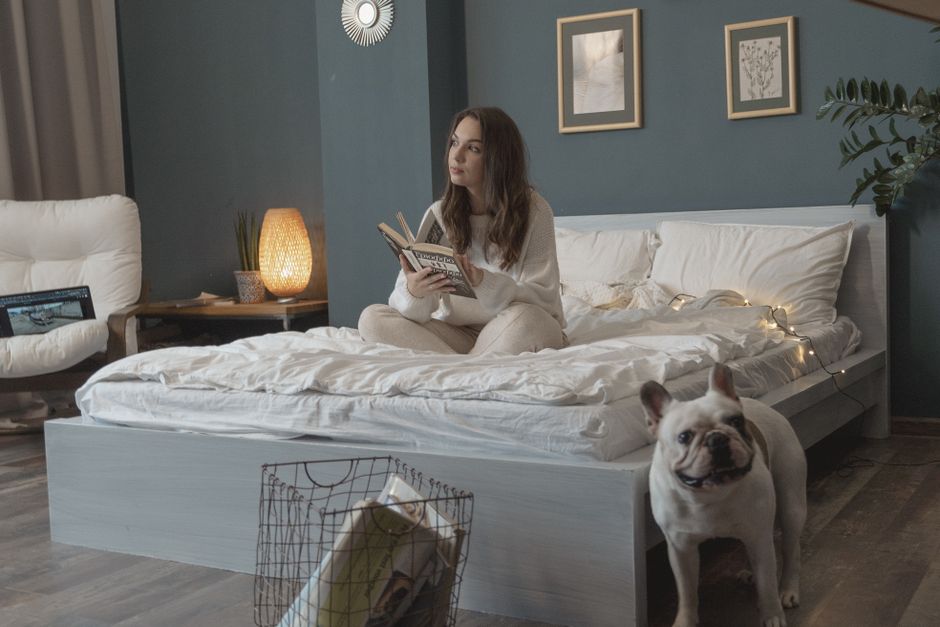 A warmly lit bedroom scene with a person reading a physical book, a mug of tea on a bedside table, and dimmed lights, creating a peaceful pre-sleep atmosphere.