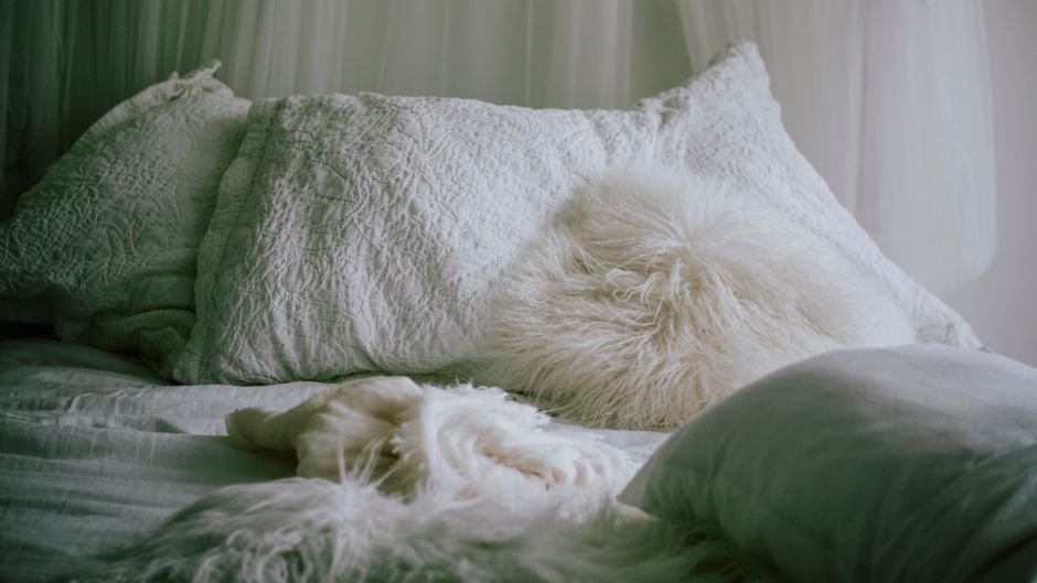 A cozy bedroom featuring layered soft textiles, plush pillows, and warm ambient lighting, creating an inviting and comfortable atmosphere.