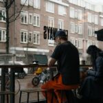 A person working on a laptop in a warmly lit cafe, looking out at a rainy city street.