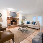 A cozy living room featuring a mix of modern and vintage furniture, a patterned rug, and potted plants, creating a personal and inviting atmosphere.