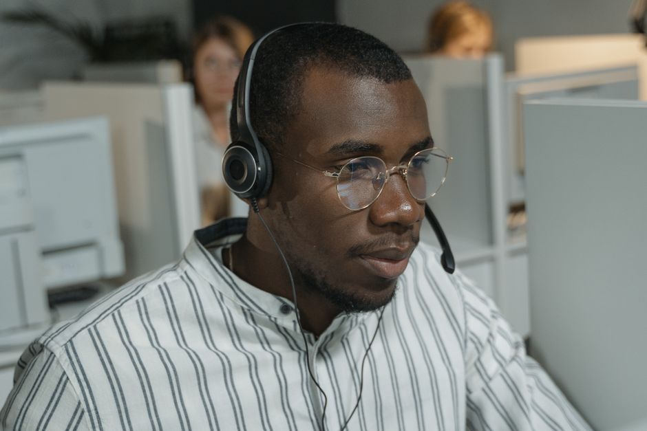 A human customer service agent, wearing a headset, smiling as they assist a customer. A transparent digital overlay with AI data points and conversation history is subtly visible, illustrating seamless AI-human collaboration.