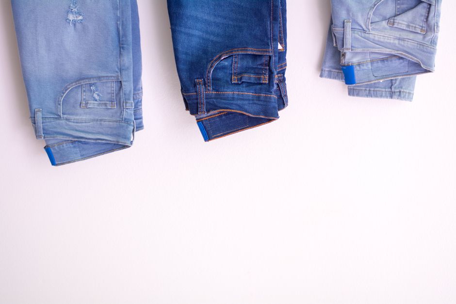 Several pairs of neatly folded dark wash and mid-wash straight-leg jeans on a rustic wooden surface, highlighting fabric texture.