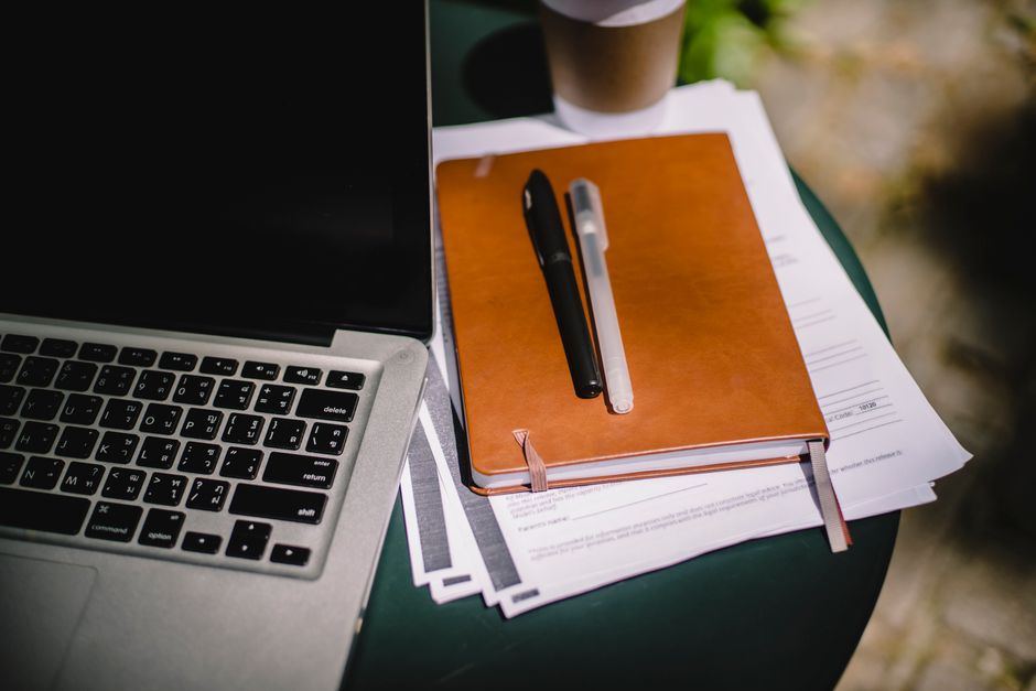 A person using a laptop with a passport and travel documents spread out, planning a trip.