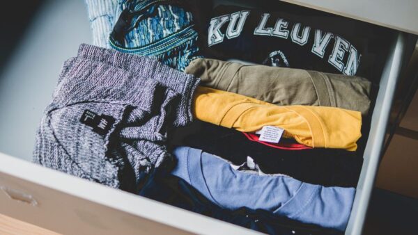 A neatly organized wardrobe featuring high-quality basic garments like white t-shirts, tailored trousers, and neutral knitwear, demonstrating smart investment in timeless pieces.