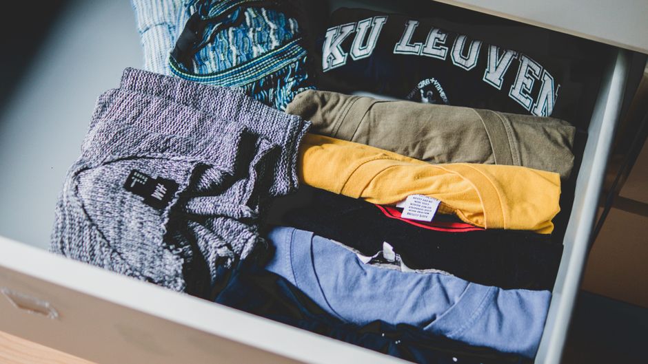 A neatly organized wardrobe featuring high-quality basic garments like white t-shirts, tailored trousers, and neutral knitwear, demonstrating smart investment in timeless pieces.