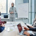 A diverse group of professionals in a modern office collaborating around a table, actively listening and engaging in discussion, while a subtle digital overlay suggests AI capturing the conversation.