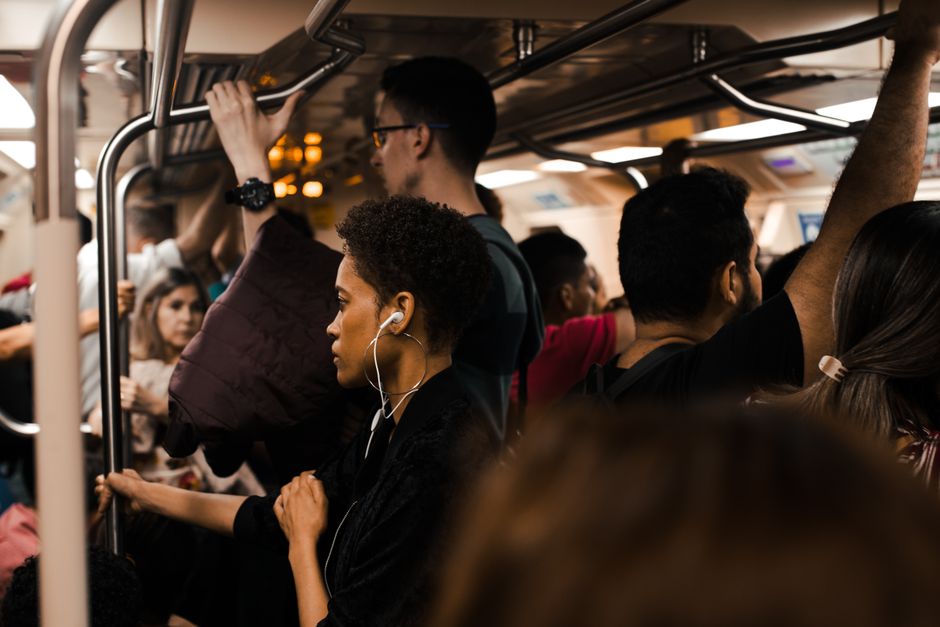 A diverse group of commuters stand and sit in a busy, modern subway car during peak hours, some reading, some looking at phones, highlighting the environment of healthy habits public transit commute.