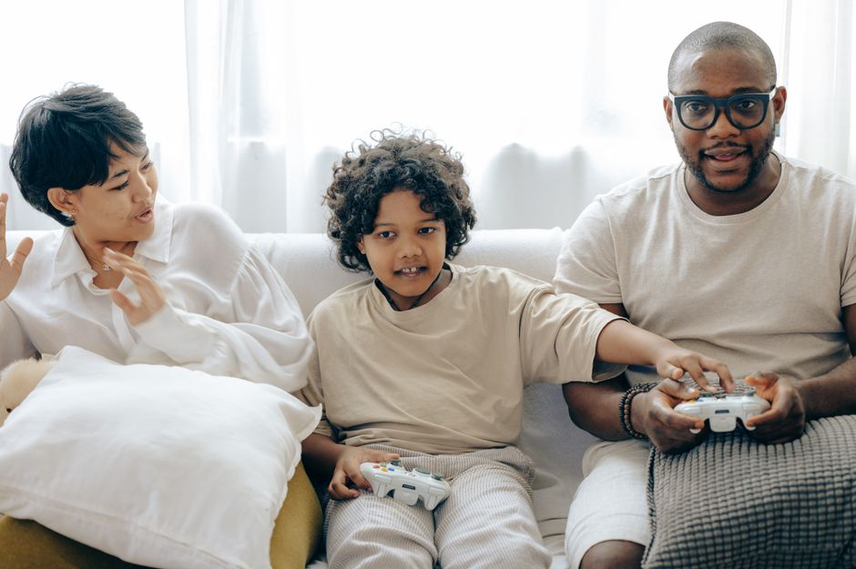 A diverse family, including parents and children, gathered around a TV, laughing and playing a video game on a console.