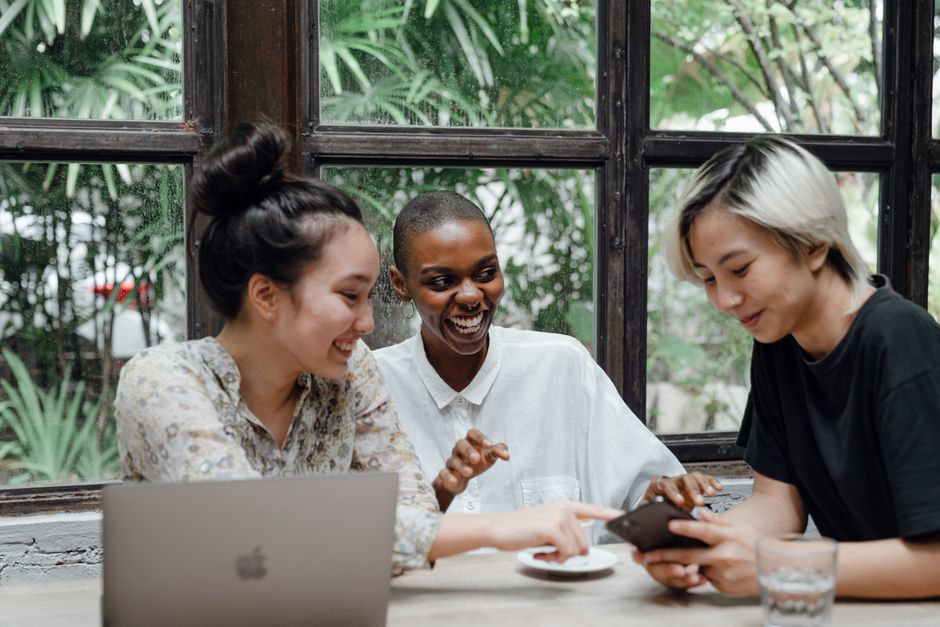 A group of diverse young adults laughing and chatting over coffee at an outdoor cafe, representing new friendships.