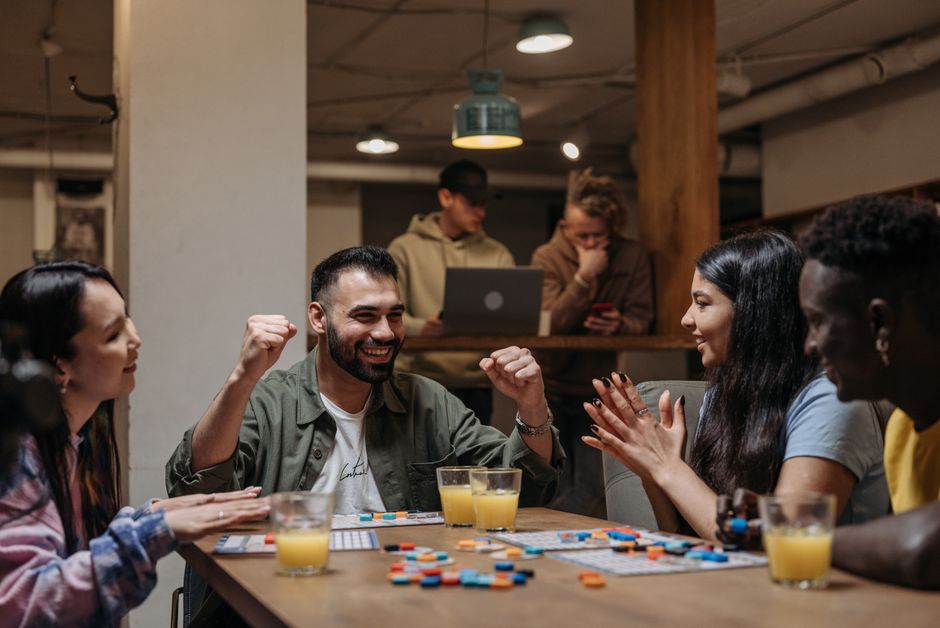 A diverse group of friends laughing and playing a board game together around a table.