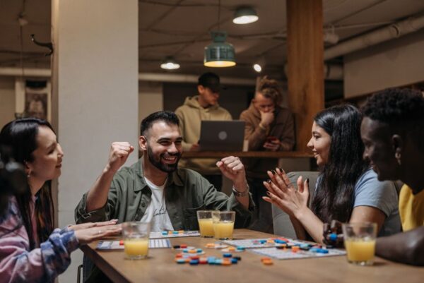 Group of diverse friends from different countries playing a digital board game on laptops and tablets, laughing and communicating via video chat.