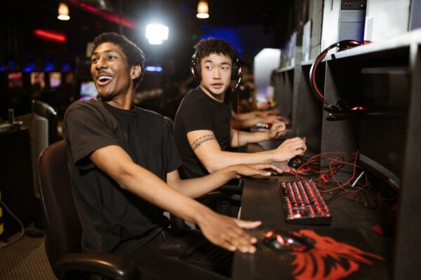 A group of diverse adult gamers wearing headsets, laughing and communicating while playing an online multiplayer game, illustrating how gaming communities can help adults make friends.