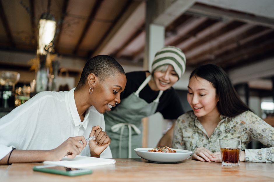 Group of diverse friends laughing and sharing a meal at a vibrant restaurant, showcasing enjoyment of social dining.
