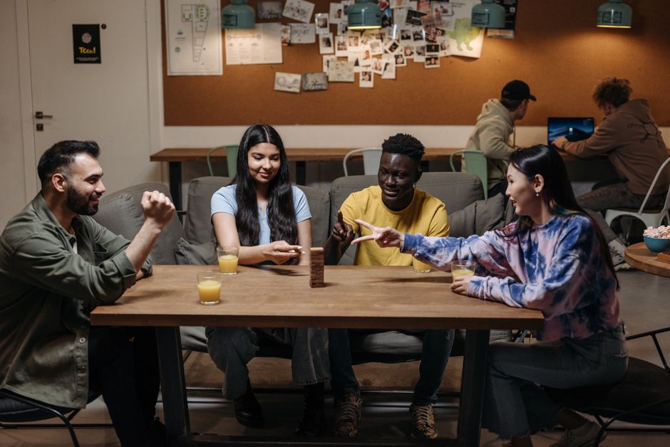 A vibrant group of university students gathered around a table, intensely focused on a strategy board game, with laptops nearby, suggesting a blend of digital and physical strategy gaming.