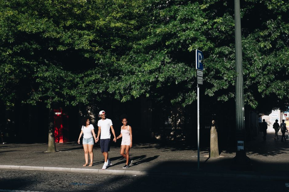 A diverse group of friends walks cheerfully down a historic cobblestone street in a European city on a warm day, some with small backpacks.