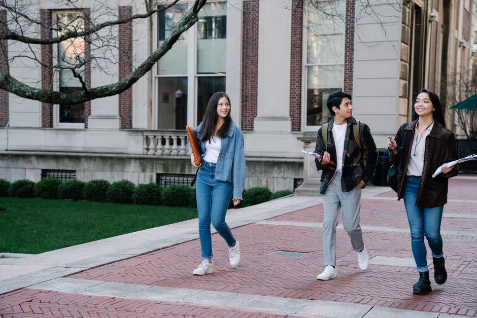 A diverse group of friends wearing various affordable spring coats – a trench, an anorak, a utility jacket – walking together in a city park during a light spring rain shower.
