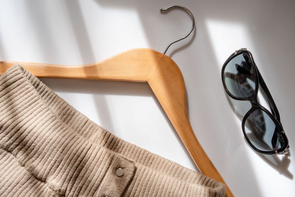 A flat lay of various neutral clothing items: a navy blazer, a white silk blouse, olive green trousers, a camel sweater, and a patterned scarf, showing mix-and-match potential.