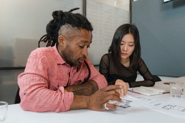 A group of diverse remote workers collaborating, one pointing at a screen displaying an AI dashboard with data visualizations, emphasizing the partnership between human teams and artificial intelligence.