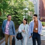 A diverse group of remote workers, some in different global locations like a park in Europe and a street in North America, all engaged in a walking meeting via headphones, demonstrating connectivity.