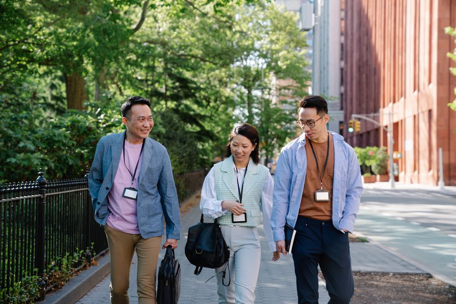 A diverse group of remote workers, some in different global locations like a park in Europe and a street in North America, all engaged in a walking meeting via headphones, demonstrating connectivity.