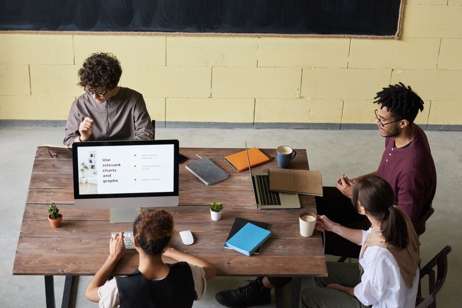 A small, diverse team in an office setting, with one person pointing at a screen showing various AI applications integrated into their workflow.